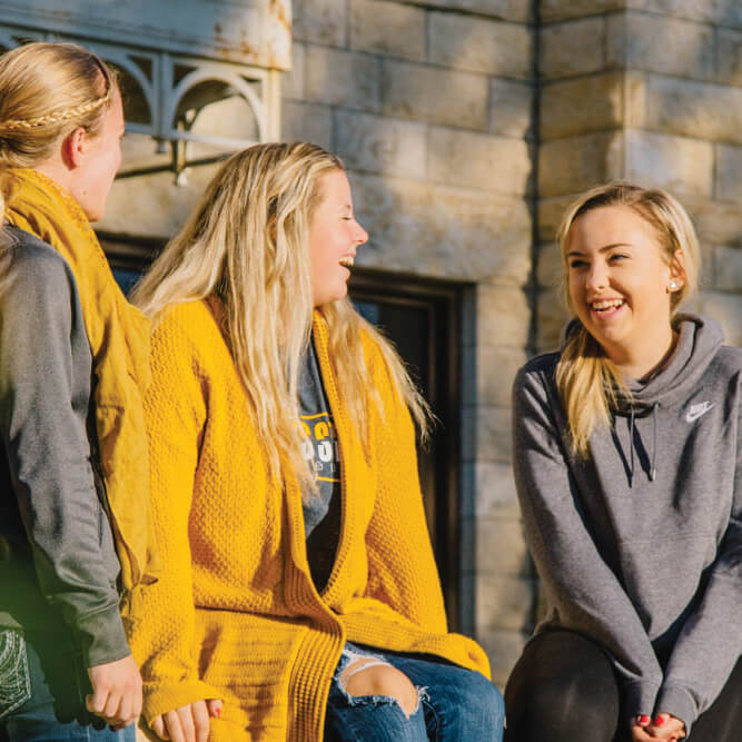 three students chatting in front of Sheridan Hall