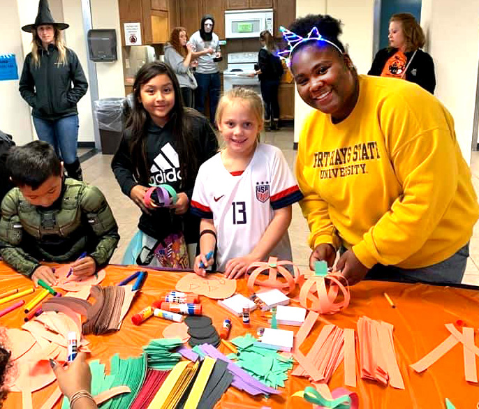 FHSU Black Student Union President Deja Brewer, right, helps children make decorations at the annual McMindes Hall Trick-or-Treat Night.