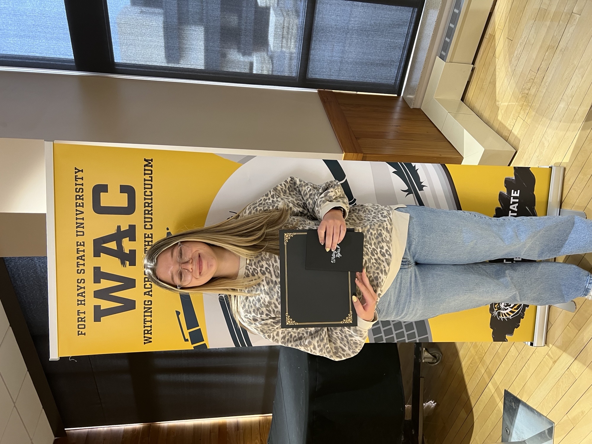 Student in white sweater holding award in front of WAC banner