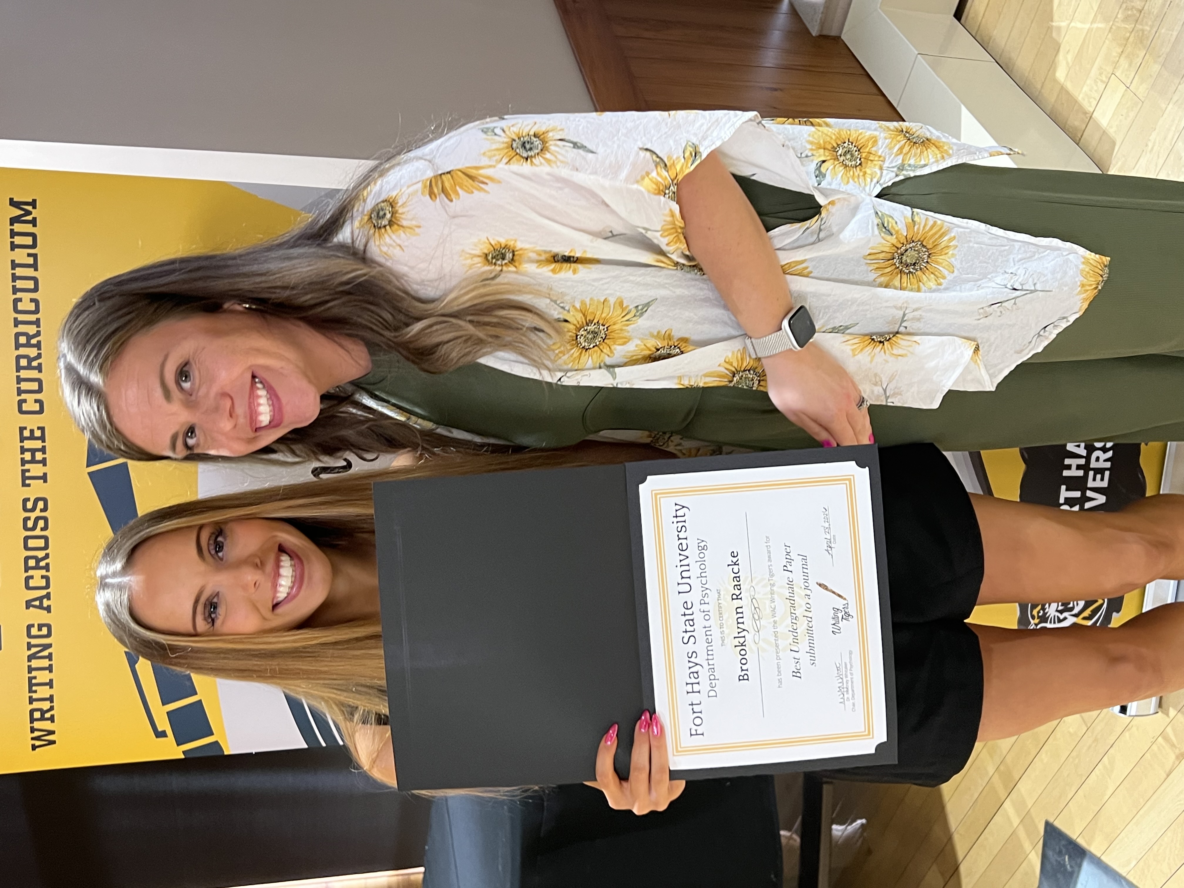 Student standing with her instructor holding award in front of WAC banner