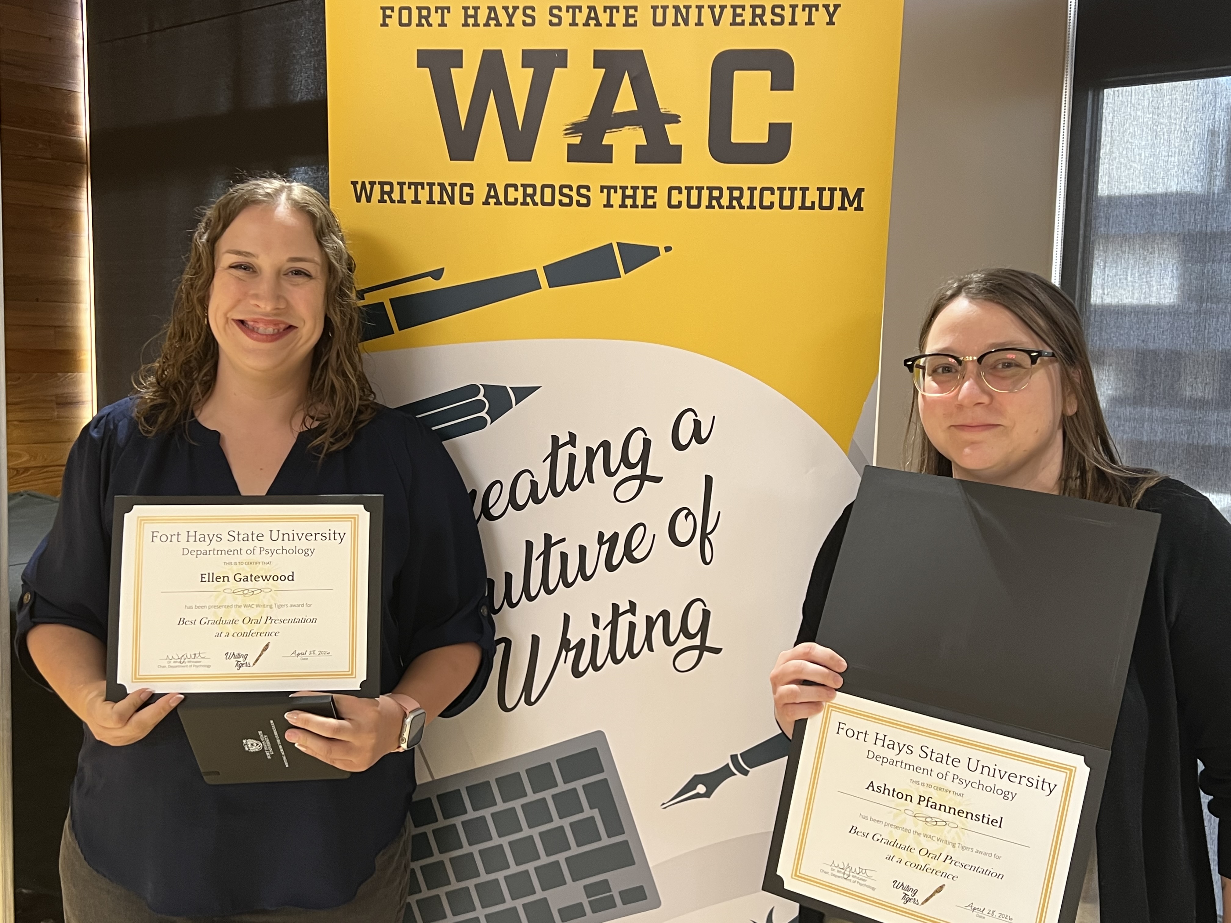 Two students standing side by side holding awards in front of WAC banner